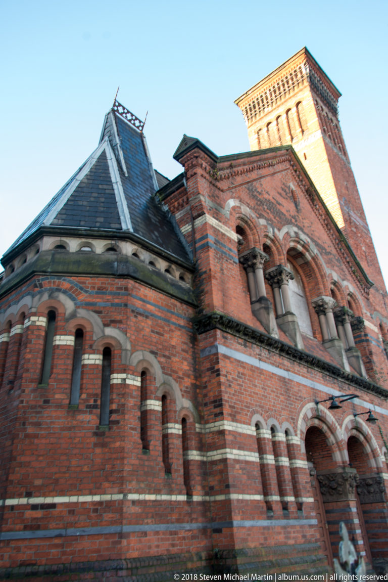 Low-angle view of a red-brick Romanesque Revival building with striped round arches and grouped windows.