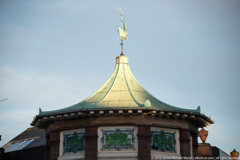 Copper-green cupola with decorative weather vane above the red masonry and colored glass of St George’s Market.
