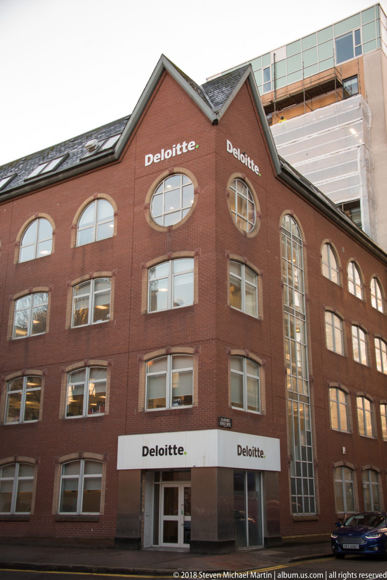 Red-brick Deloitte office with broad gables, round-arched windows, and a tall central glazed stair bay.