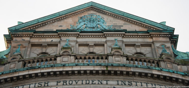 Triangular pediment of the Scottish Provident Institution with a large crest, sculptural figures, balustrade, and green-patinated trim.