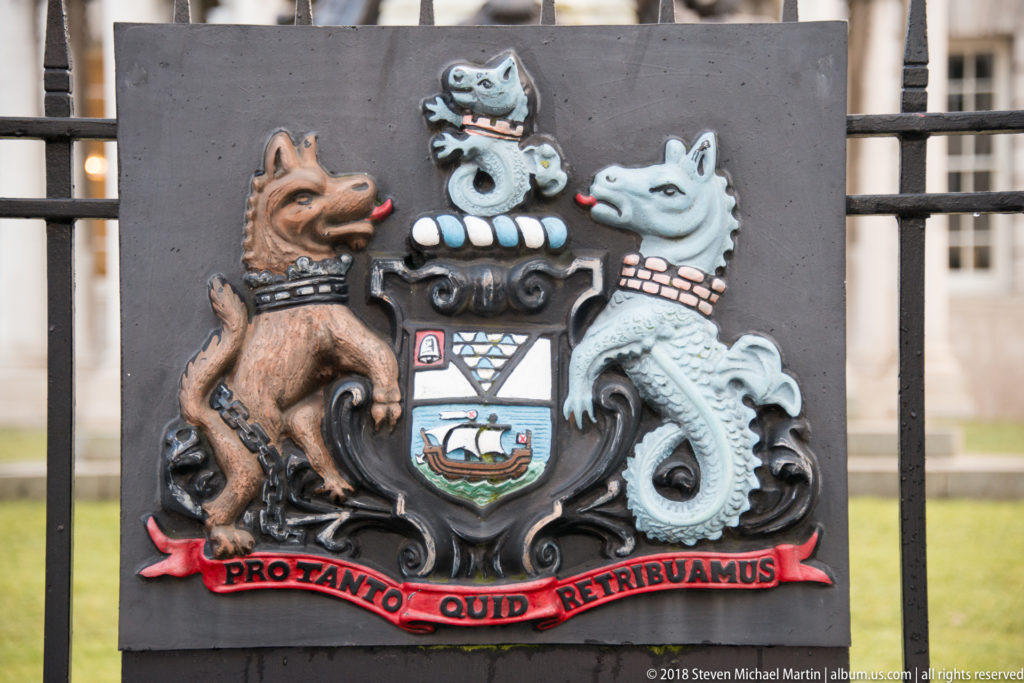 Painted Belfast coat of arms plaque with ship shield, two animal supporters, crest, and red Latin motto scroll.