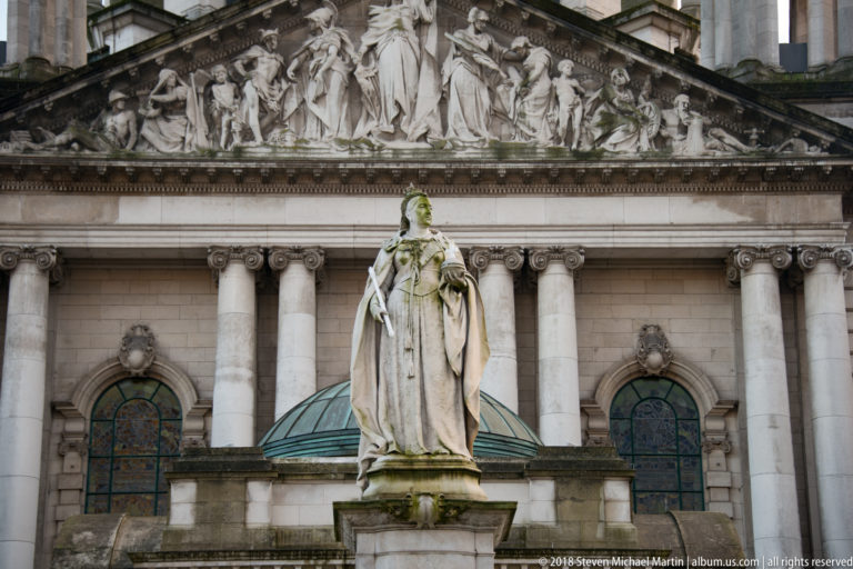 Sir Thomas Brock’s marble Queen Victoria Memorial standing before the columned façade and sculpted pediment of Belfast City Hall.