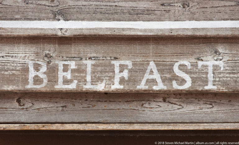 White BELFAST lettering painted across weathered horizontal wooden planks.