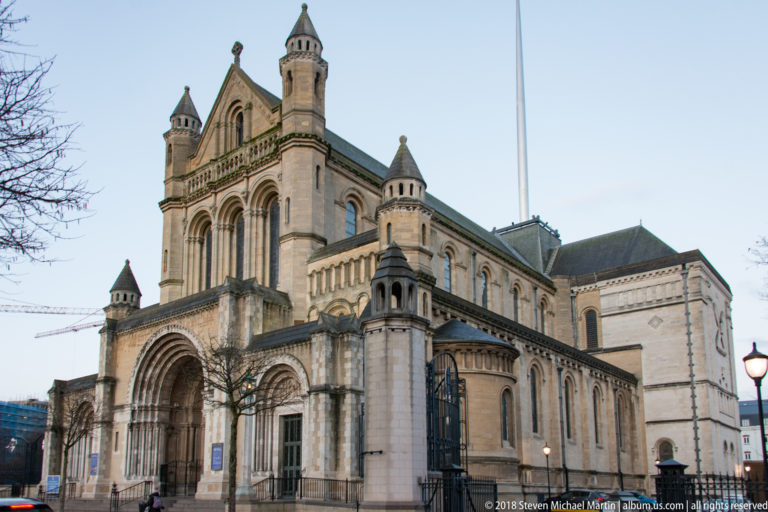 Oblique exterior view of St Anne's Cathedral with round arches, pale stone walls, and corner turrets.