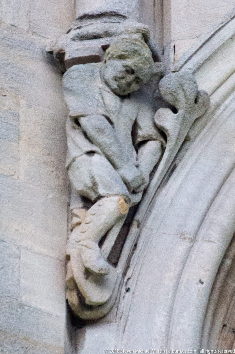 Weathered crouching stone grotesque carved into the curve of an arch at St Anne's Cathedral.