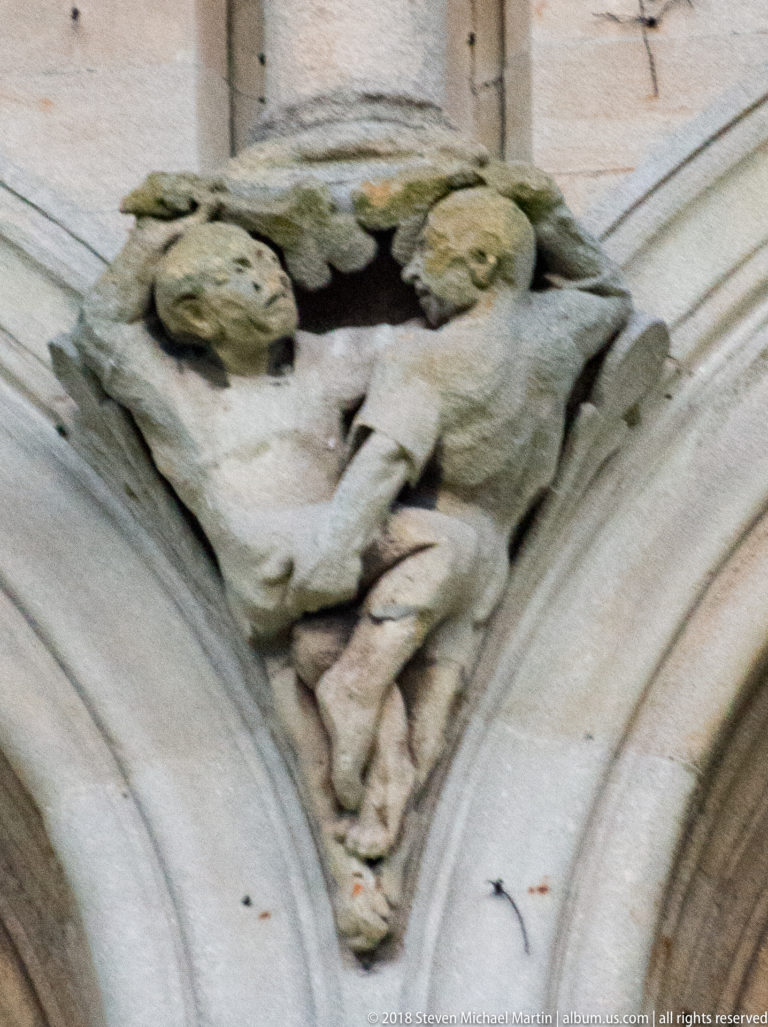 Crouching weathered grotesque set into a triangular stone recess beside an arch at St Anne's Cathedral.