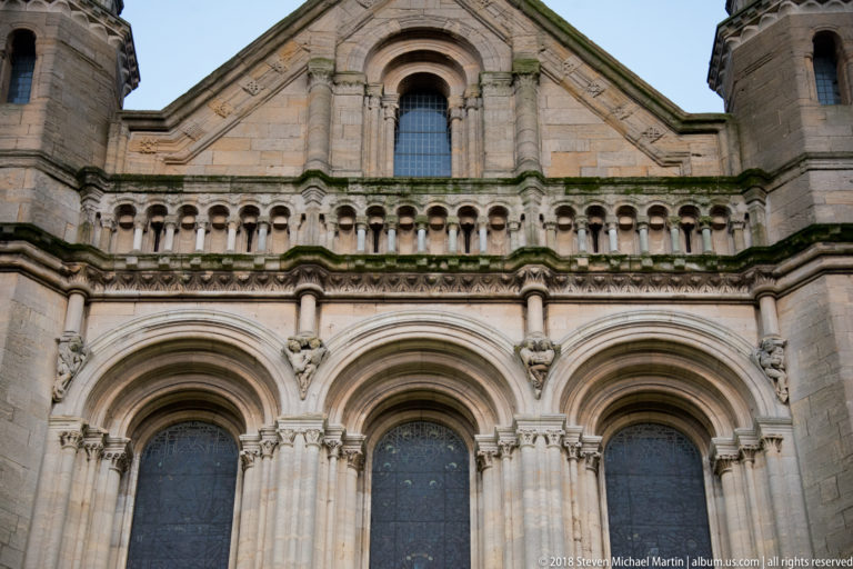 Upper façade of St Anne's Cathedral with three tall arched windows, arcading, and a gabled roofline.
