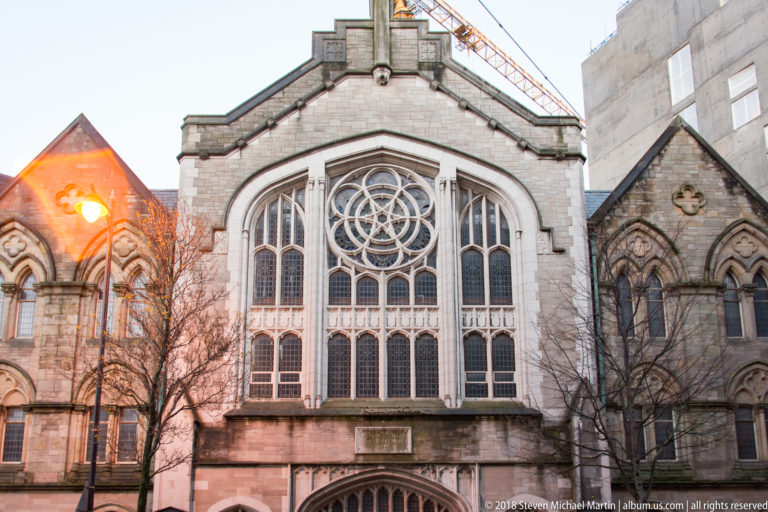 Historic Belfast church façade with a large circular traceried window and flanking Gothic windows.