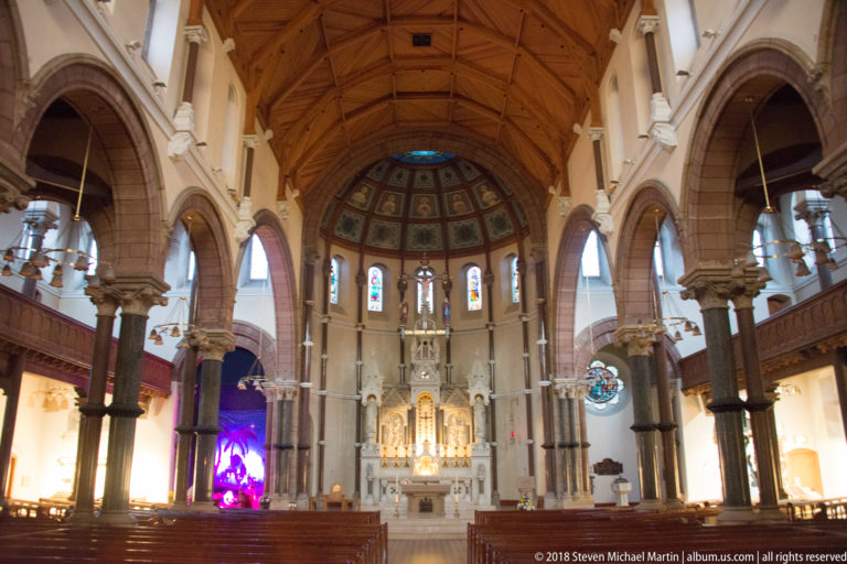 Nave of St Patrick’s Church, Belfast, looking through red-sandstone arches and granite columns toward the high altar and apse.