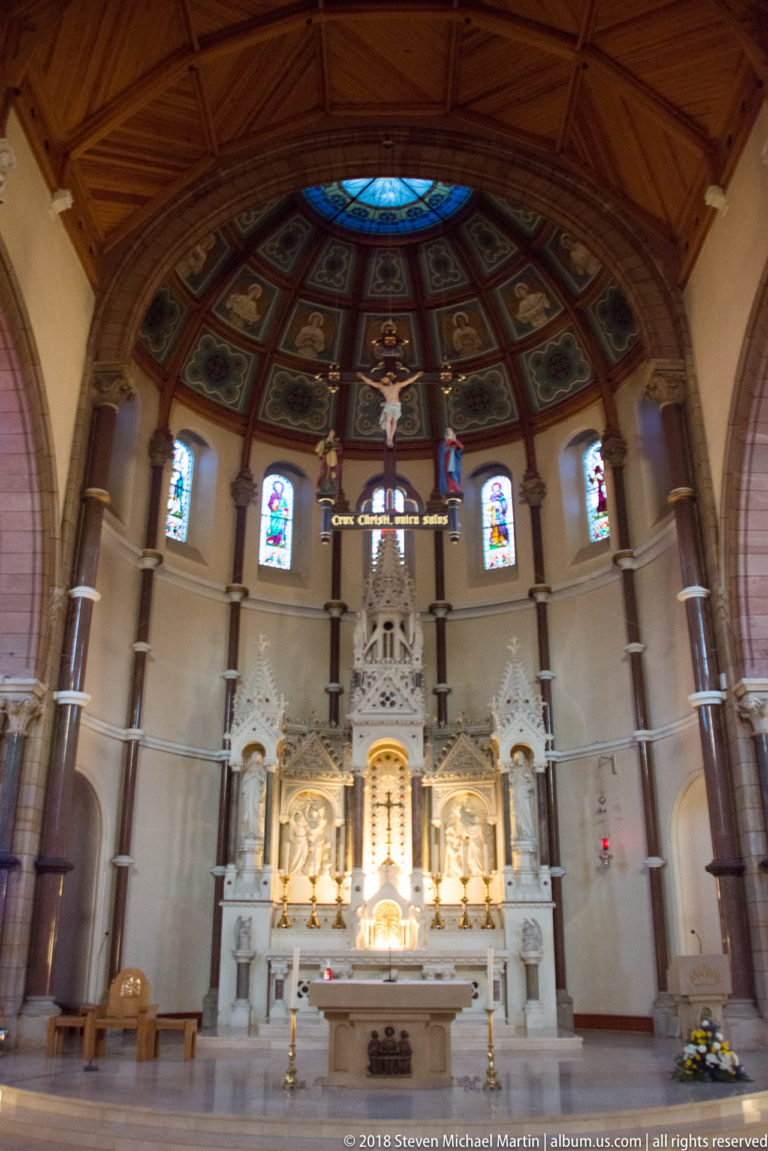 High altar and reredos of St Patrick’s Church beneath the decorated apse, with stained-glass lancets and a freestanding altar in front.