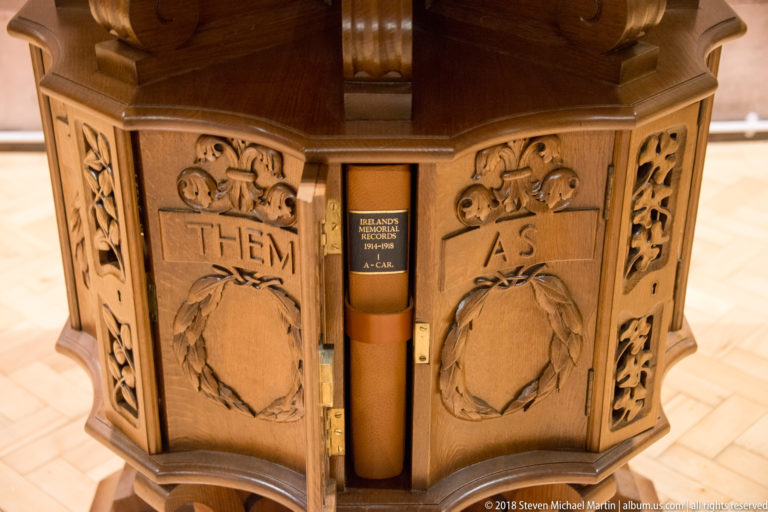 Carved wooden church furnishing with wreath motifs, Gothic tracery, inscribed panels, and a central bound volume.