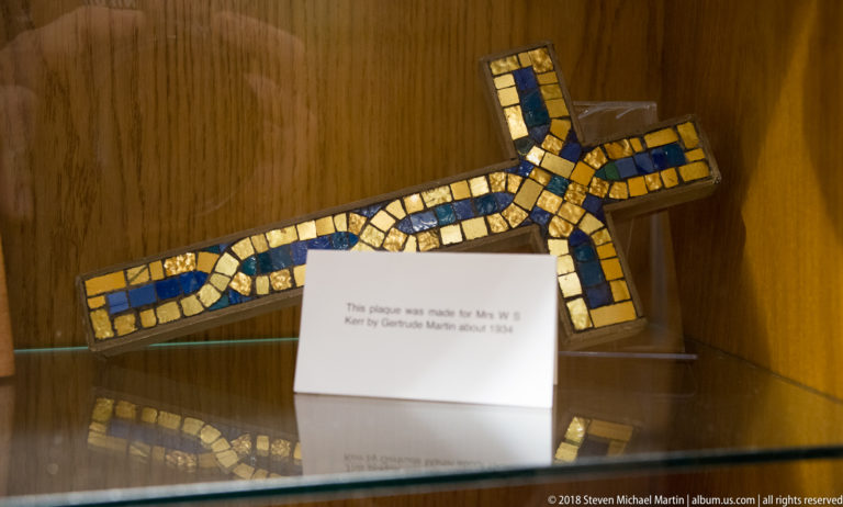 Cross-shaped plaque covered with alternating blue and gold mosaic tesserae in a glass case.