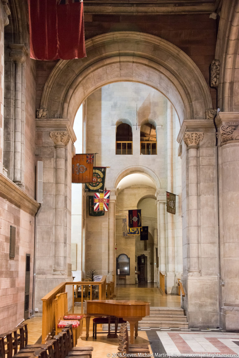 Large stone arch opening into a cathedral interior with seating, a raised platform, and hanging standards.