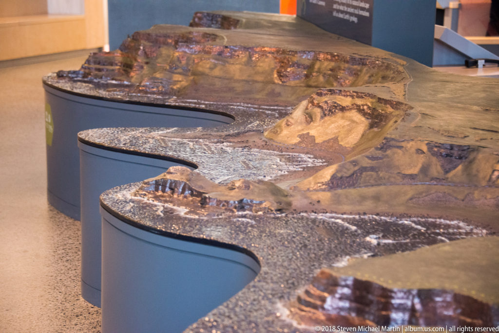 Raised three-dimensional coastal terrain model displayed on a curved interpretive table inside the visitor centre.