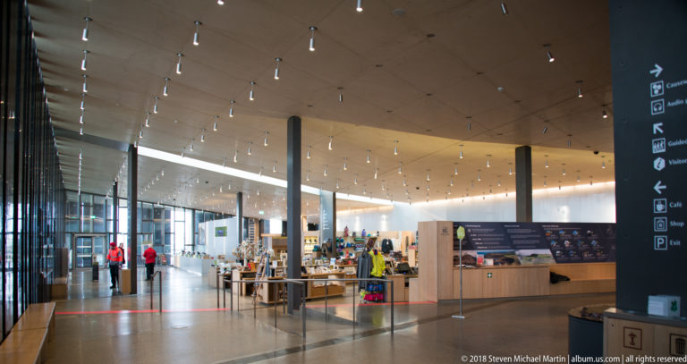 Spacious visitor-centre hall with retail displays, information areas, glass walls, and rows of ceiling lights.