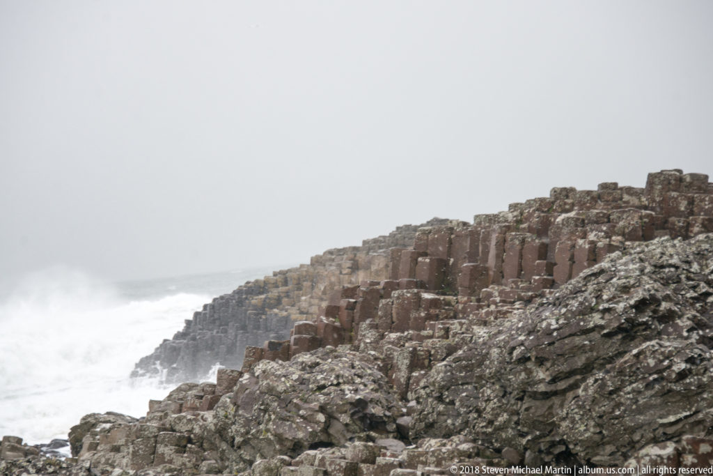 Rows of polygonal basalt columns rising behind rough volcanic rocks beside the gray Atlantic.