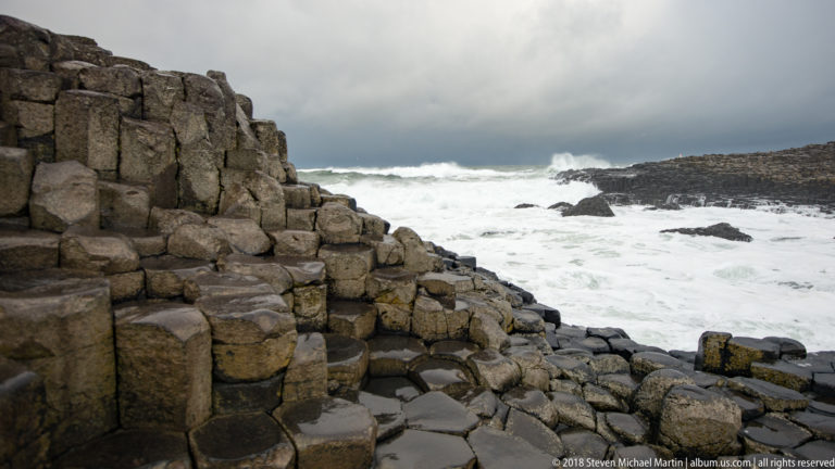 Tall vertical basalt columns beside shorter blocks and tide pools, with white Atlantic surf beyond.