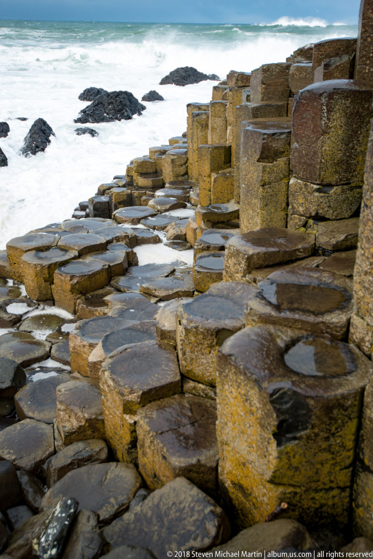 Low wet basalt columns forming natural steps beside taller columns and foaming Atlantic water.