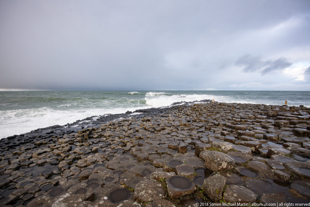 Broad wet basalt pavement extending to the Atlantic surf beneath a dark gray winter sky.