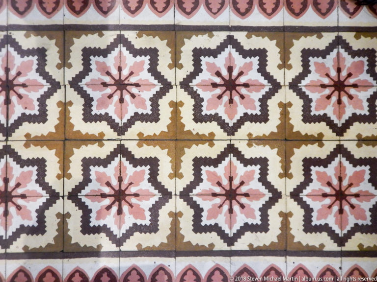 Close view of repeating pink, cream, brown, and black geometric floor tiles with star-shaped motifs.