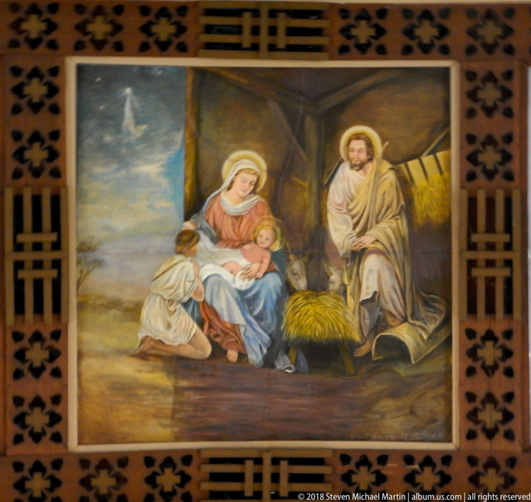 Nativity painting with Mary holding the infant Jesus, Joseph standing nearby, and a kneeling figure beside the child.