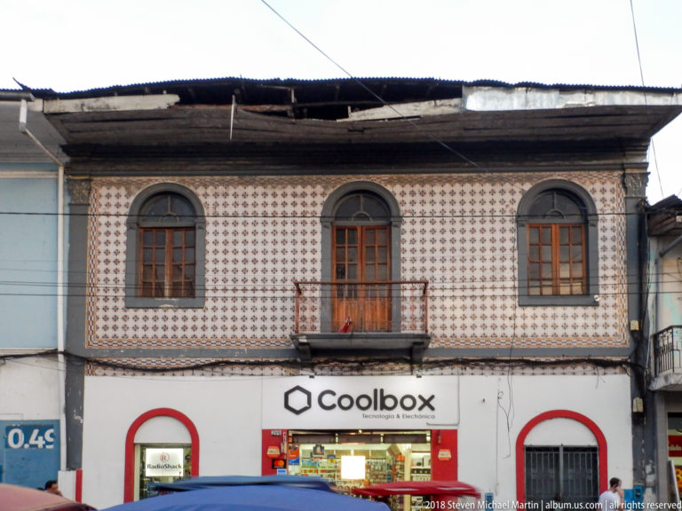 Patterned tiled upper façade with arched windows and central balcony above a modern Coolbox storefront.