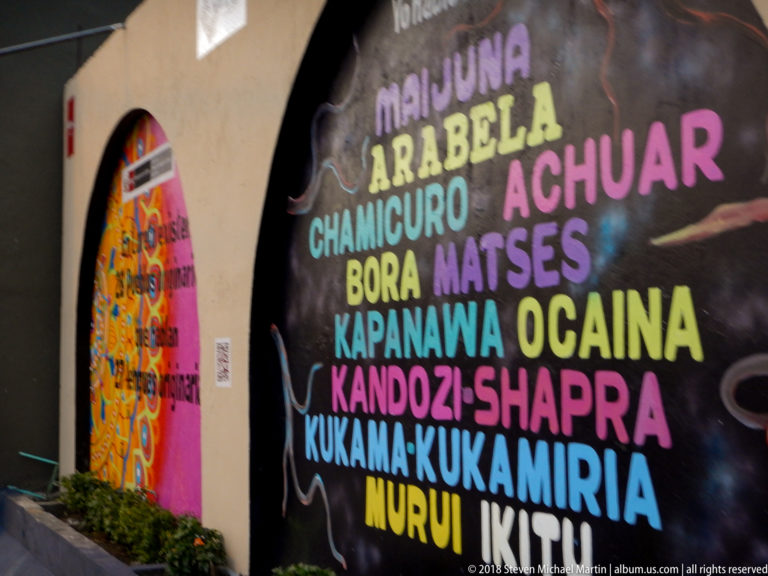 Dark mural with multicolored names including Maijuna, Arabela, Achuar, Bora, Matsés, Ocaina, Kukama-Kukamiria, and Ikitu.