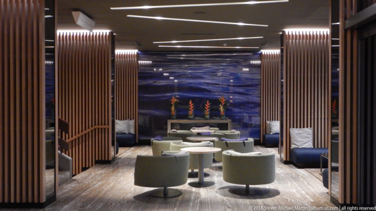 Symmetrical hotel lounge with pale green chairs, wood screens, blue wall treatment, and orange tropical flowers.