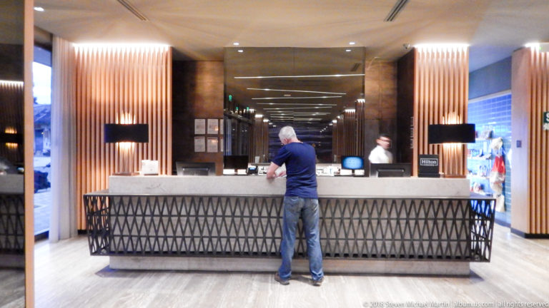 Traveler standing at a hotel reception counter framed by illuminated vertical wood panels.