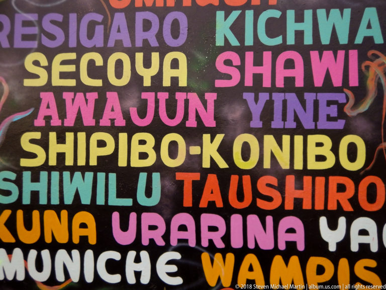 Colorful mural of large words including Kichwa, Secoya, Shawi, Yine, Shipibo-Konibo, Taushiro, Urarina, and Muniche.