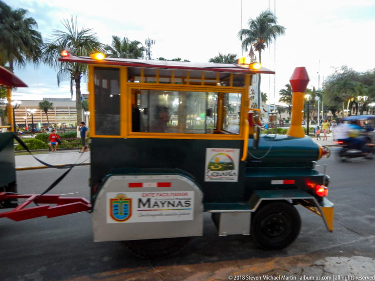 Side view of green-and-orange locomotive-shaped road train marked Municipalidad Provincial de Maynas.