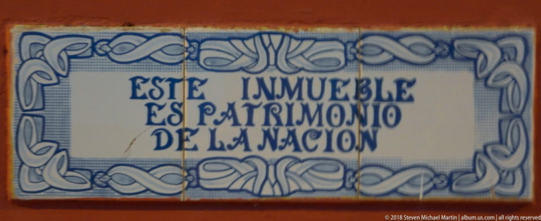 Blue-and-white ceramic plaque reading “Este inmueble es patrimonio de la nación” within a decorative border.