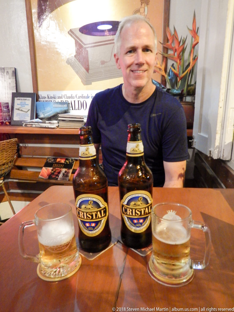 Smiling man seated at a table behind two Cristal beer bottles and glass mugs.