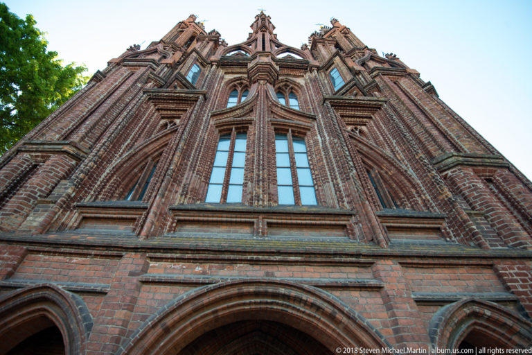 Low-angle red-brick Gothic façade with pointed arches, tall windows, molded ribs, and clustered pinnacles.