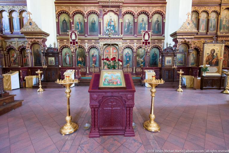 Frontal iconostasis with central icon lectern and two tall brass candle stands in the cathedral nave.