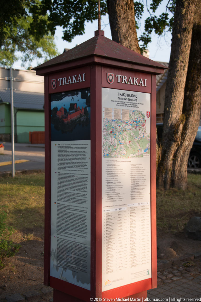 Red visitor-information kiosk labeled TRAKAI with map and interpretive panels beside a large tree.