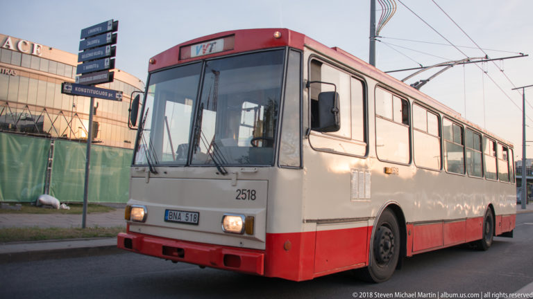 Red-and-cream trolleybus on a Vilnius street beneath overhead electric wires, viewed from the front-left corner.