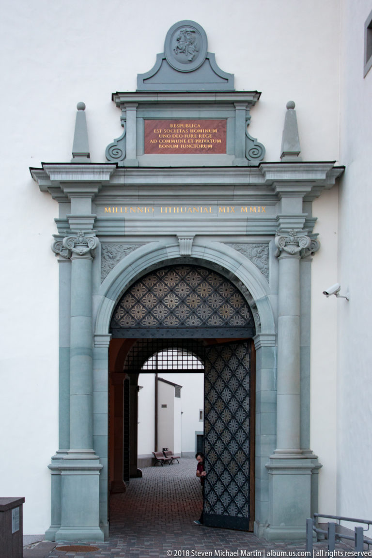 Open patterned metal gate within an ornate stone portal, revealing a paved courtyard beyond.