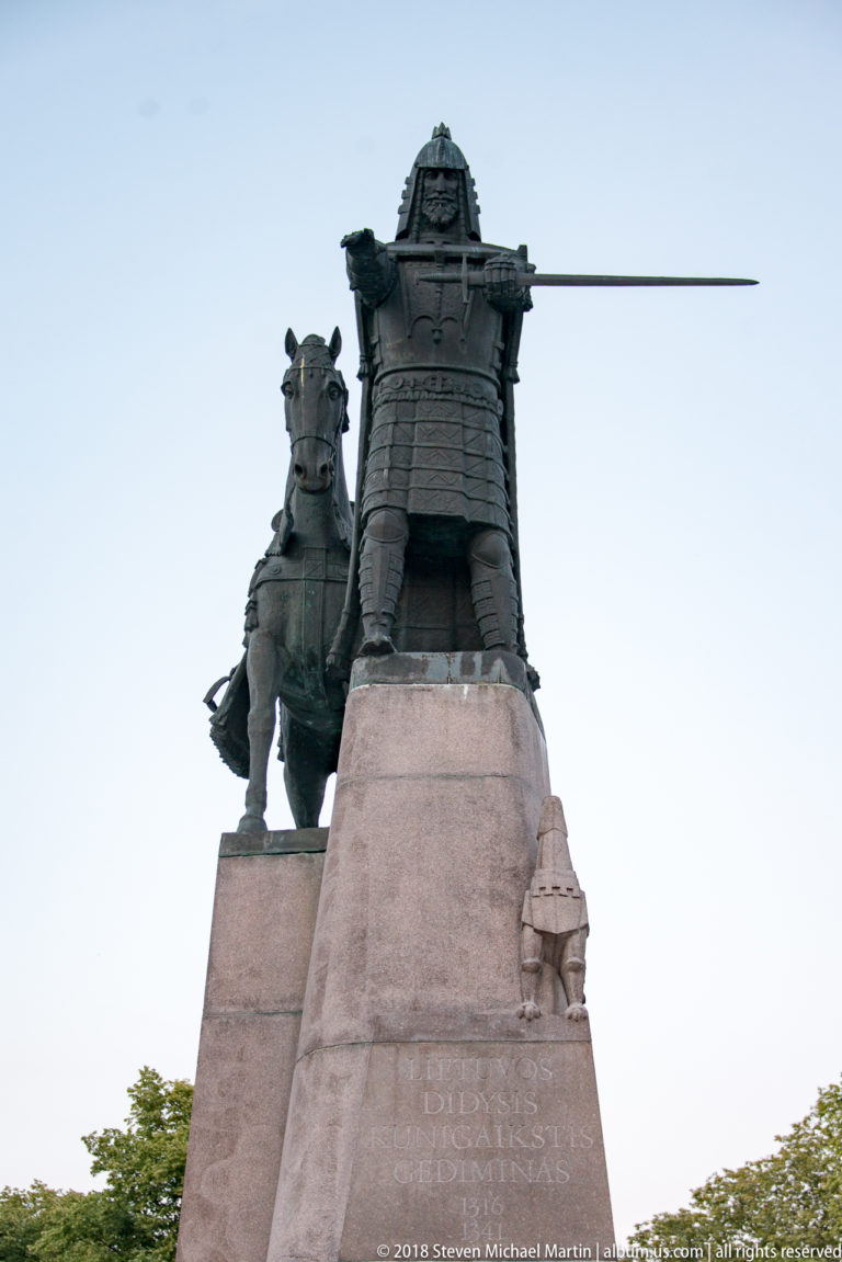 Bronze equestrian monument to King Mindaugas on a tall stone pedestal, viewed dramatically from below.