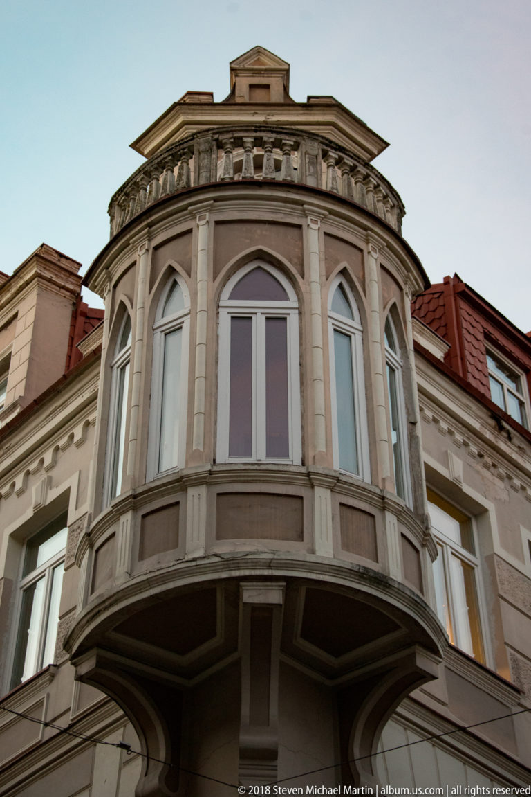 Rounded upper-story bay window with tall panes, classical moldings, and heavy brackets on a historic Vilnius townhouse.