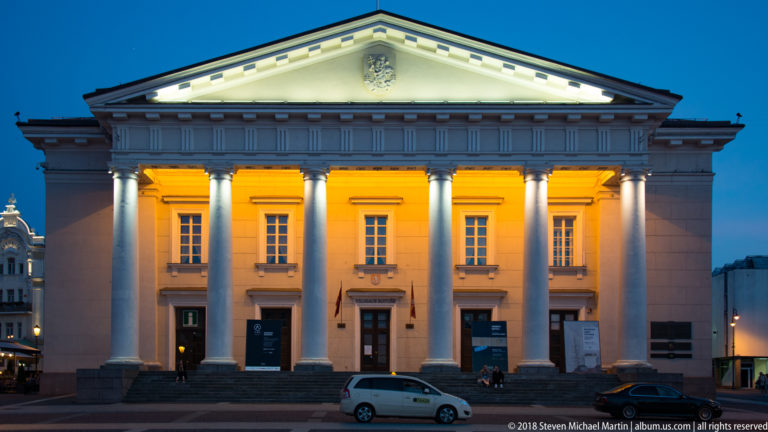 Illuminated neoclassical Vilnius Town Hall with tall front columns, triangular pediment, and symmetrical façade at night.