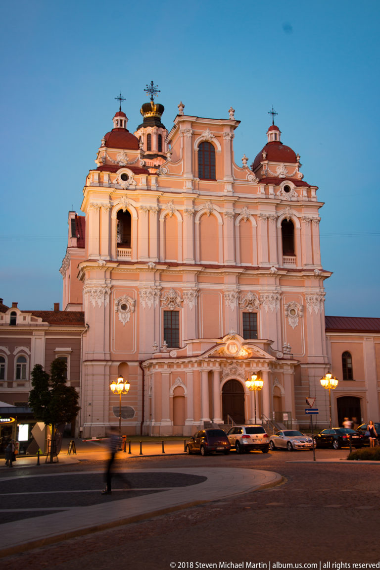 Wide dusk view of the pink Baroque Church of St. Casimir with domed corner towers and crown-topped central lantern.