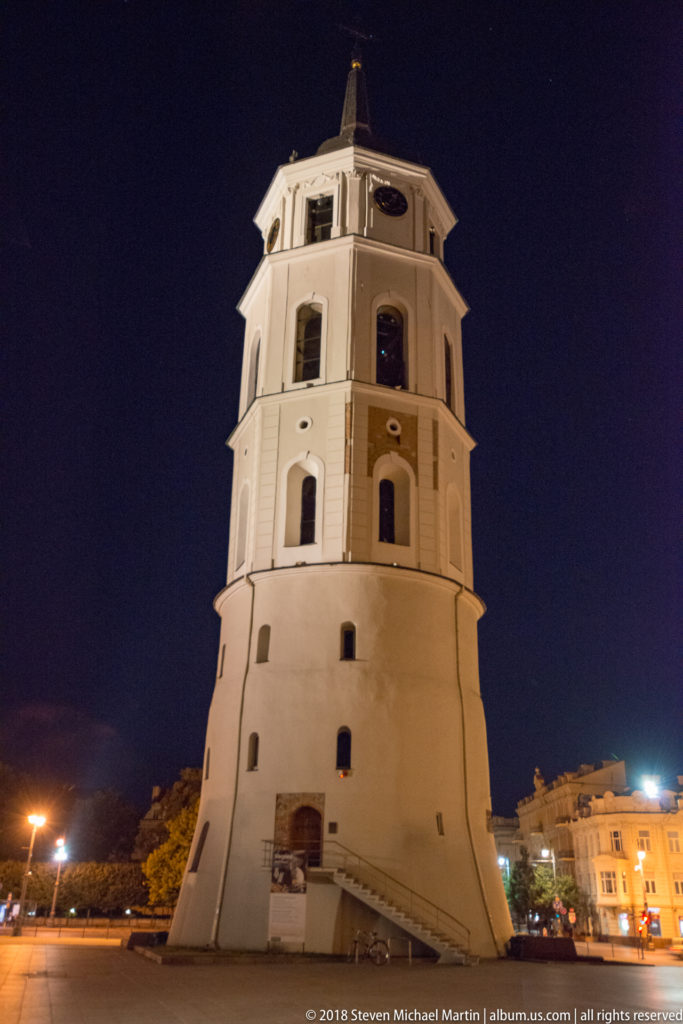 Freestanding white bell tower of Vilnius Cathedral, seen from below at night with octagonal upper stages and small windows.