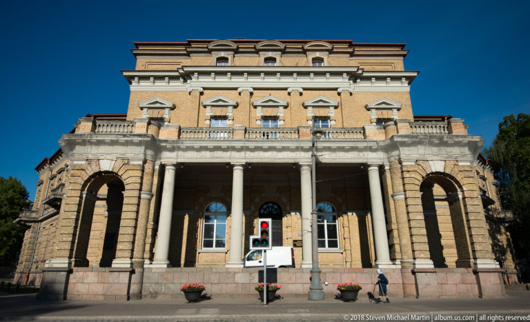 Historic civic building with rusticated stone base, deep arcades, colonnaded balcony, pedimented windows, and traffic signal.