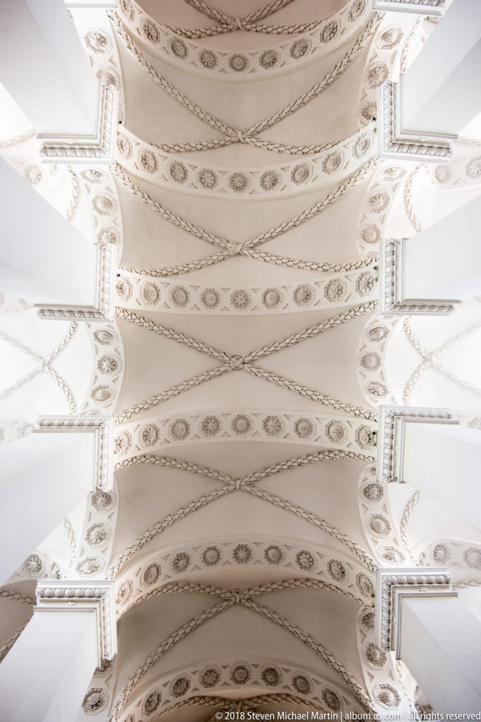 White barrel vaults with rosettes, garlands, molded borders, and square piers inside Vilnius Cathedral.