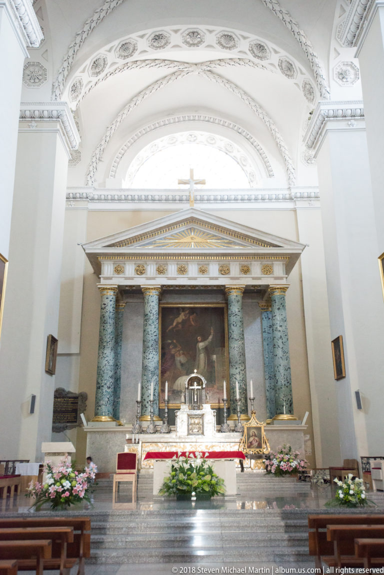 Vilnius Cathedral high altar with green-marble columns, triangular pediment, central painting, gilded cross, and flowers.