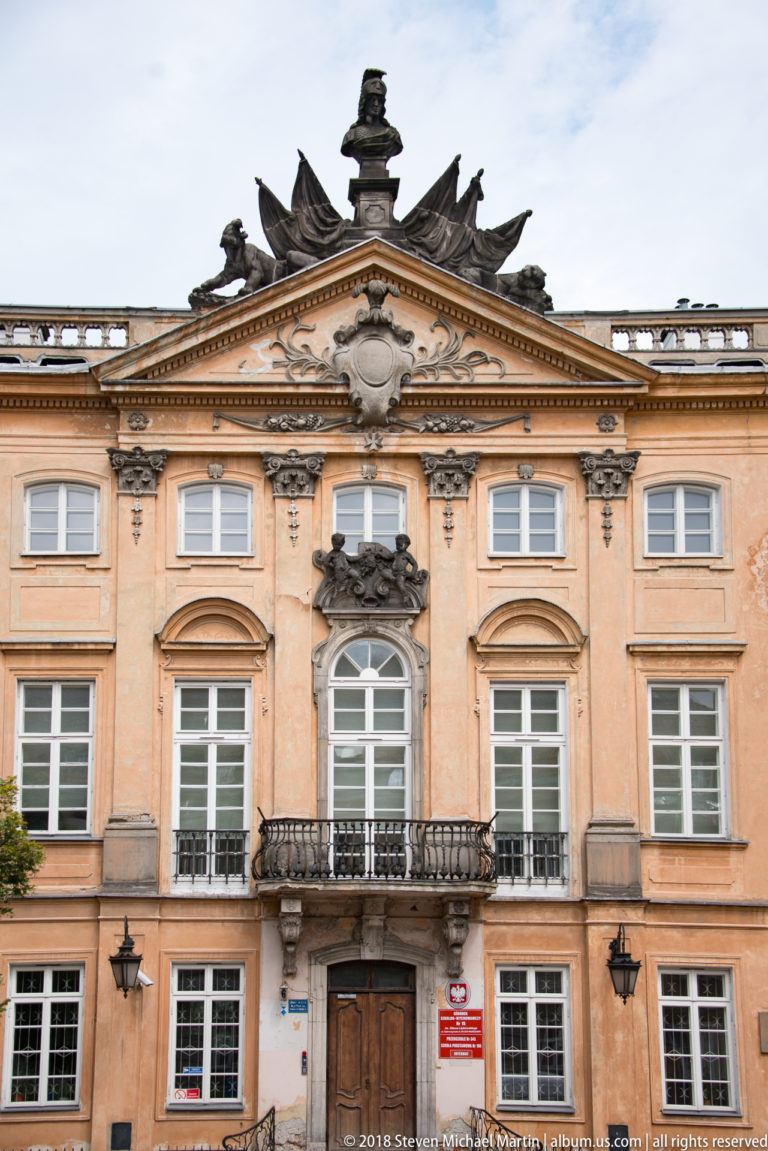 Peach historic palace facade with stone balcony, carved cartouche, sculpted pediment, and classical window surrounds.