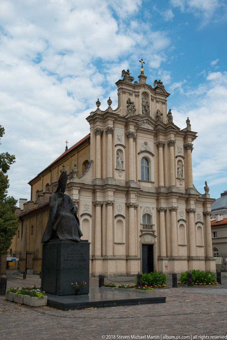 Dark bronze bust monument on a stone pedestal in front of an ornate pale Baroque church facade.