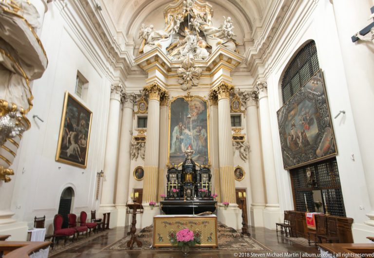 Elaborate white-and-gold church sanctuary with tall columns, large paintings, and a flower-decorated altar table.