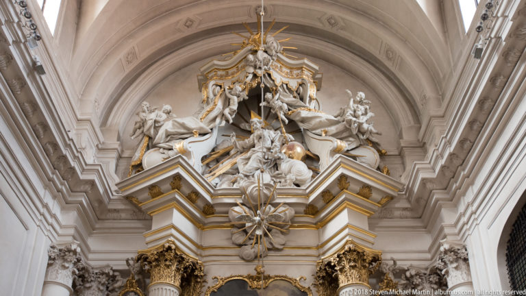 White and gilded Rococo stucco figures and ornament rise above the sanctuary beneath a pale vaulted ceiling.